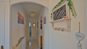 Un pasillo con piso de baldosas blancas, un marco de puerta de madera y una pequeña pizarra sobre un estante con un letrero con forma de corazón debajo.