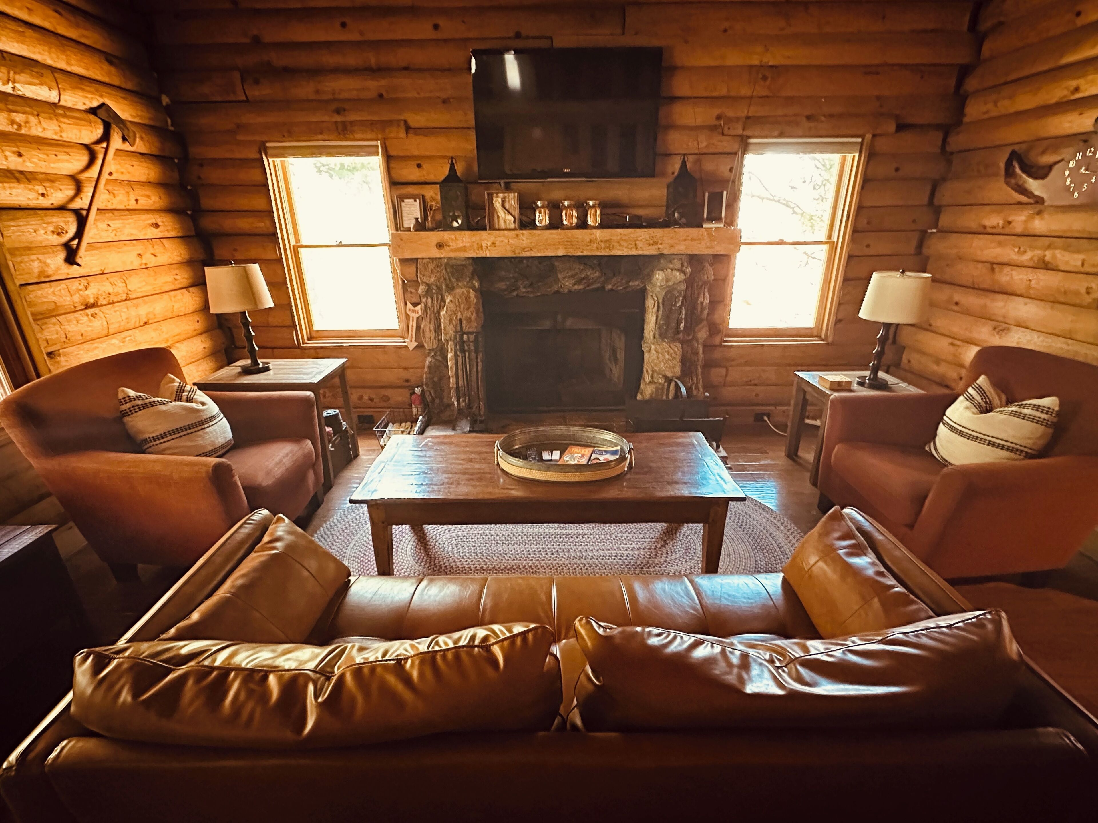 Un interior de cabaña acogedor con chimenea de piedra, sofás de cuero y un televisor montado encima.