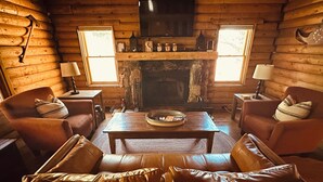 A cozy cabin interior with a stone fireplace, leather sofas, and a television mounted above it. - Cozy Idyllwild Log Cabin w/ A/C & EV Charger (Idyllwild)