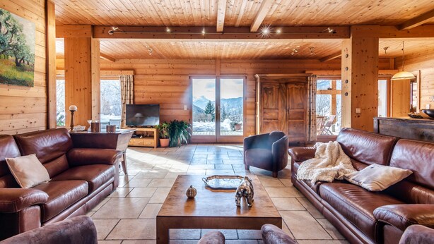 Un intérieur spacieux en bois, avec des canapés en cuir, une table basse et une grande fenêtre donnant sur une vue imprenable sur les montagnes.