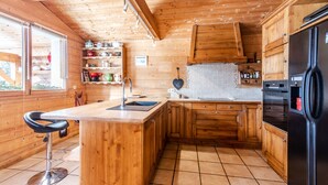Une cuisine rustique, située dans une cabane en bois, avec un îlot central, des armoires en bois et un réfrigérateur noir.
