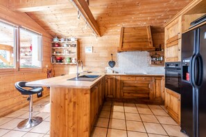 A wooden cabin kitchen with a central island, wooden cabinets, and a black refrigerator.