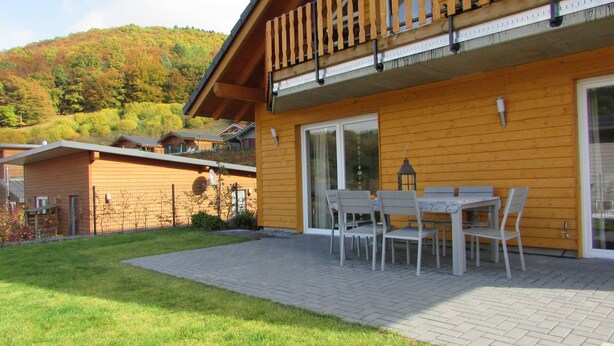 Un edificio de madera con un balcón, un patio con mesa y sillas, y vistas a una colina.
