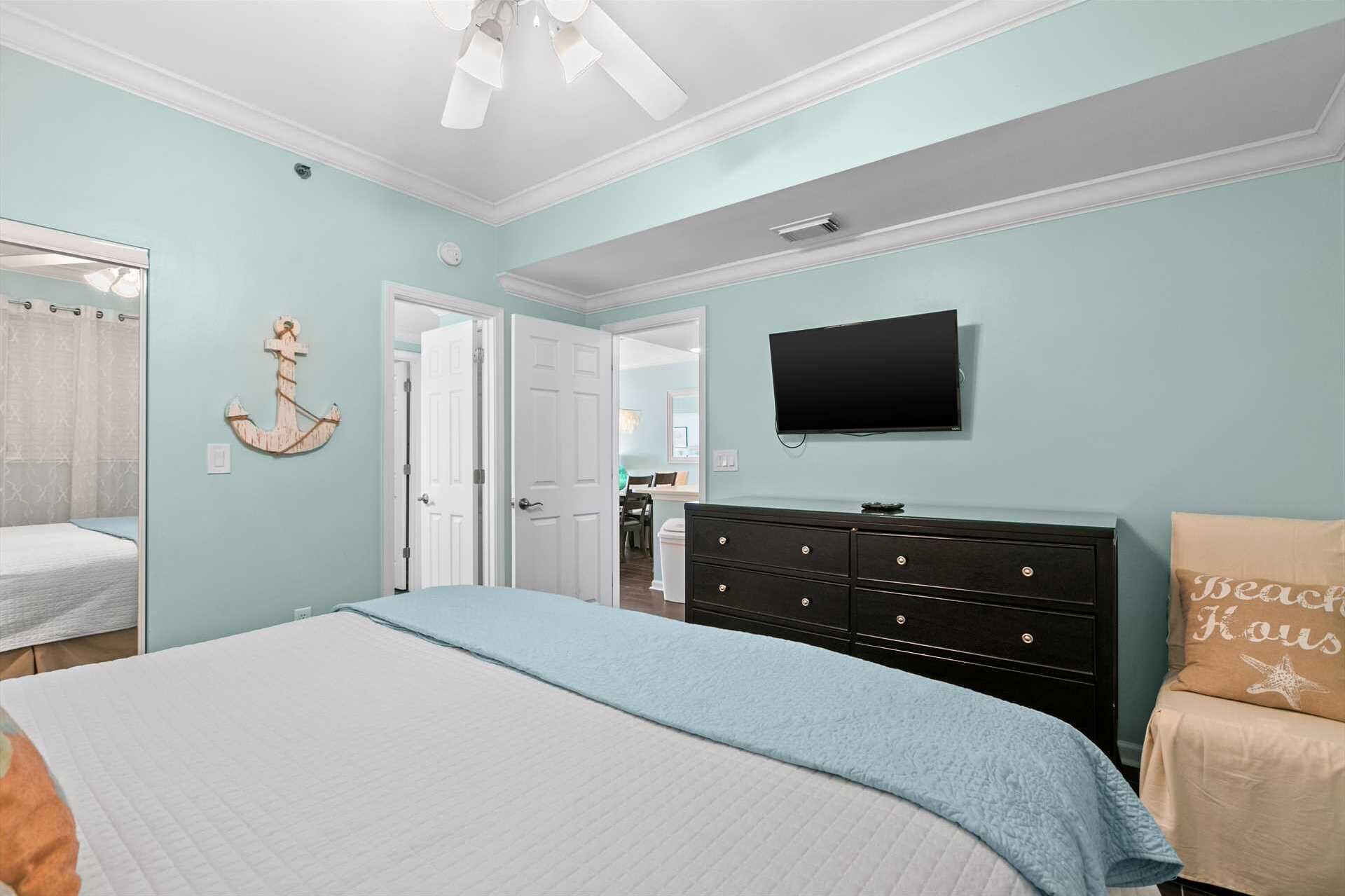A bedroom with a bed, a dresser, a television, and a door leading to another room.