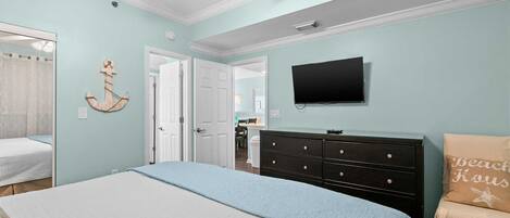 A bedroom with a bed, a dresser, a television, and a door leading to another room.