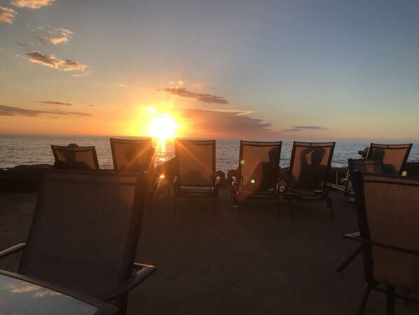Un área de estar frente al océano con sillas durante la puesta de sol.