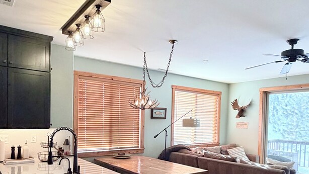 A modern kitchen with a central island, dark cabinets, and a dining area with a sofa and a ceiling fan.