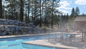A swimming pool with a stone wall, lounge chairs, and a view of trees.