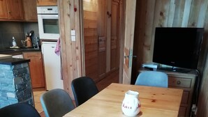 Una mesa de madera con sillas, un televisor y una pared de piedra en una habitación acogedora.