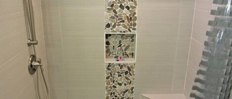 A shower with a mosaic tile wall, a showerhead, and a handheld shower attachment.