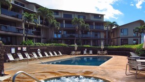 A pool area with lounge chairs and a hot tub, surrounded by a building with balconies and palm trees. -  Now with AC!    Ocean View  2 bd 2 Bath, 1 story condo at the Makahuena. (Poipu Beach)