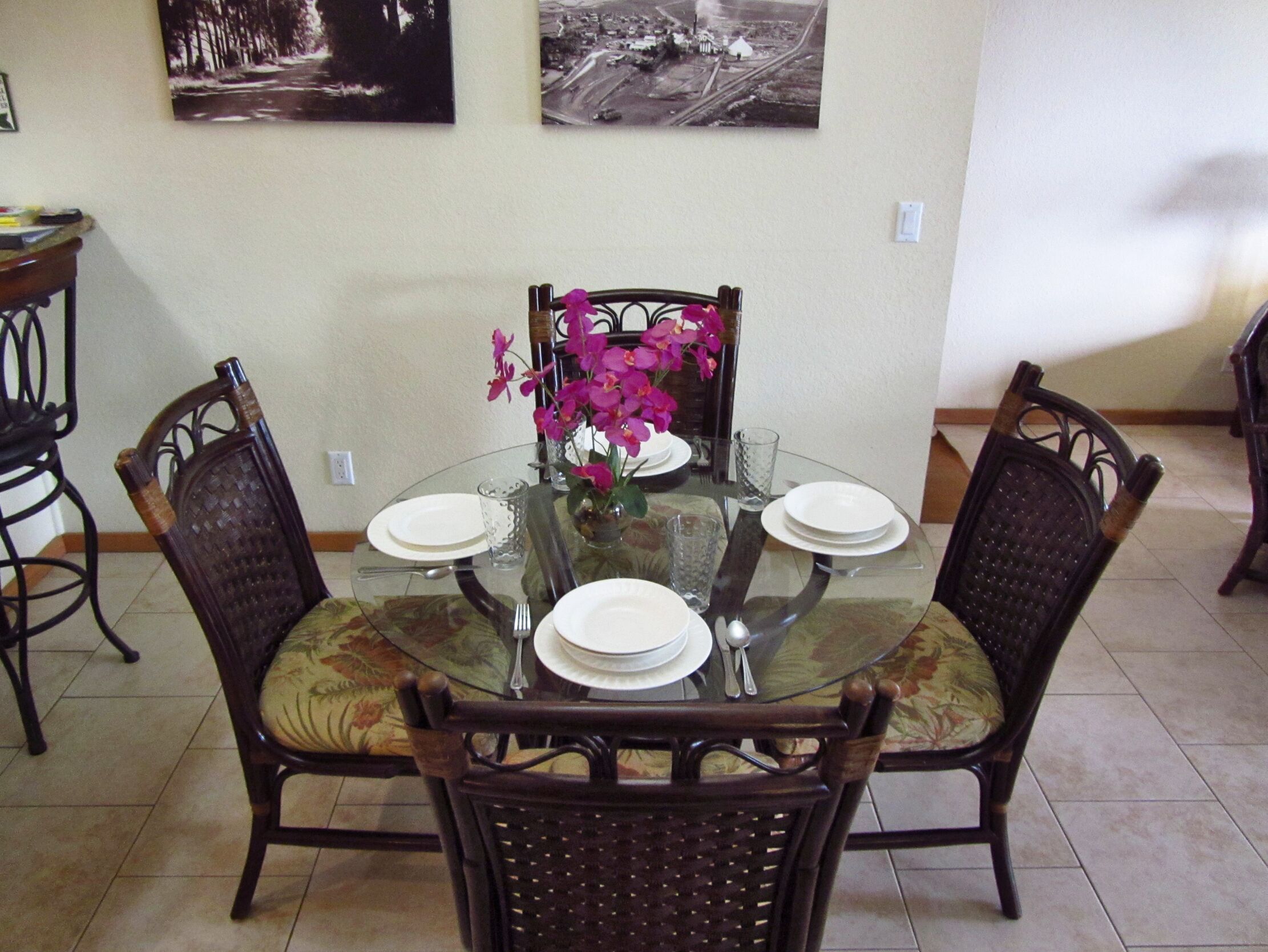 A dining table with four chairs, a vase with flowers, and two framed pictures on the wall.