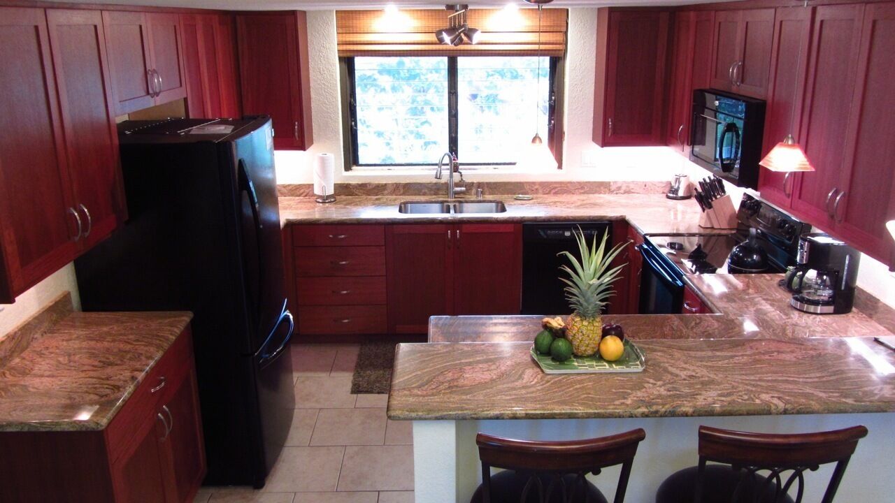 A kitchen with red cabinets, a black refrigerator, a sink, and a countertop with a fruit bowl.