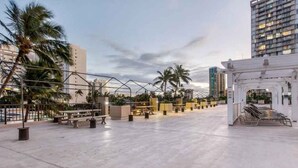 Eine Dachterrasse mit Sitzbereichen, Palmen und modernen Gebäuden im Hintergrund.