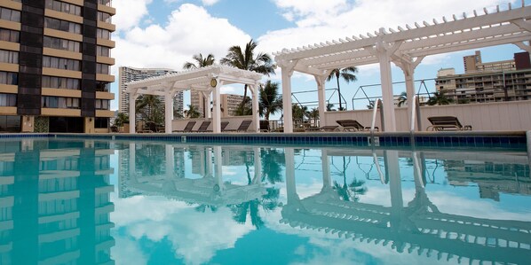 A swimming pool with a clear blue water surface, surrounded by lounge chairs and a white pergola structure.