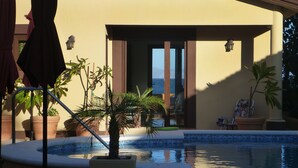 Un espace piscine offrant une vue sur l’océan, agrémenté de plantes en pot et d’un fauteuil de relaxation.