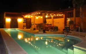 A swimming pool with a lounge area, including chairs and tables, and a covered seating area with string lights.