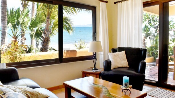 Une pièce avec vue sur la plage, un canapé noir, une table basse en bois et une lampe.