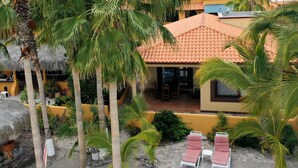 Un complexe hôtelier tropical doté de palmiers, d’une structure à toit de chaume et d’un bâtiment à toit de tuiles avec des chaises longues.