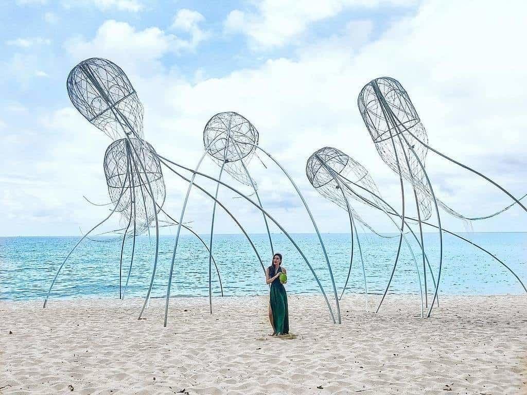 A beach with a person standing in front of abstract wire sculptures.