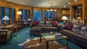A cozy cabin interior with a large sectional sofa, a glass coffee table, and a cowhide rug. There are wooden walls, a dining area, and a kitchen with wooden cabinets. - Explore Colorado! VeryPrivate. Peaceful, AlpineLuxury on 3 Acres. 2 MilesToTown (Breckenridge)