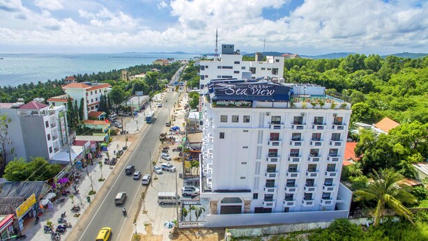 A multi-story hotel with a prominent 'Sea View' sign, a busy street with vehicles, and a coastal backdrop. - Levan Hotel (Phu Quoc)
