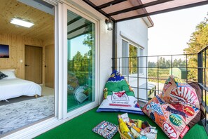 A room with a bed, a large window, and a balcony with snacks and a beach life pillow.