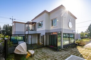 A modern two-story house with a balcony, large windows, and a covered outdoor seating area.