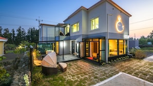Uma casa moderna de dois andares, com fachada de vidro, varanda e interior bem iluminado.
