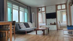 A living room with a sofa, wooden coffee table, and a TV mounted on the wall. - JejuMermuri (Seogwipo)