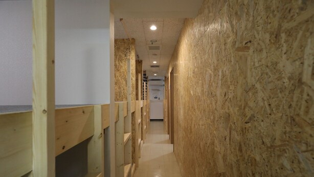 A narrow hallway with wooden walls and a tiled floor, leading to a room with a white door. - Odori Backpackers (Sapporo)