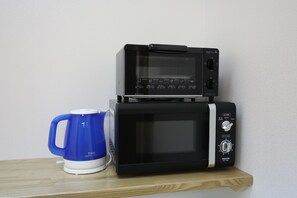 A black microwave oven with a digital display and control panel, placed on a wooden shelf. - Odori Backpackers (Sapporo)