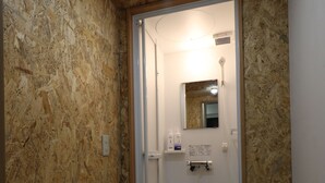 A bathroom with a shower, a mirror, and a shelf with toiletries. - Odori Backpackers (Sapporo)