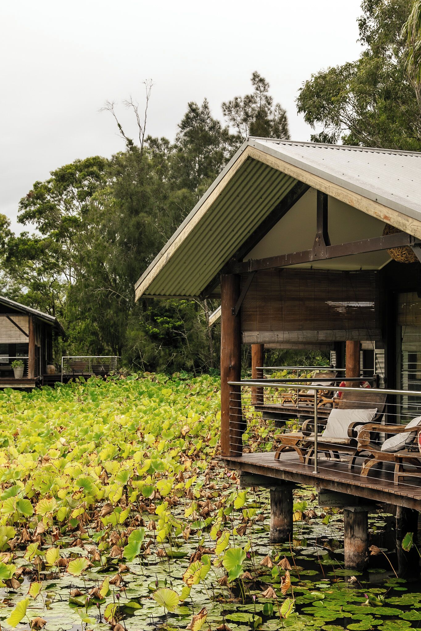 A wooden structure with a covered deck over water, surrounded by lush greenery.