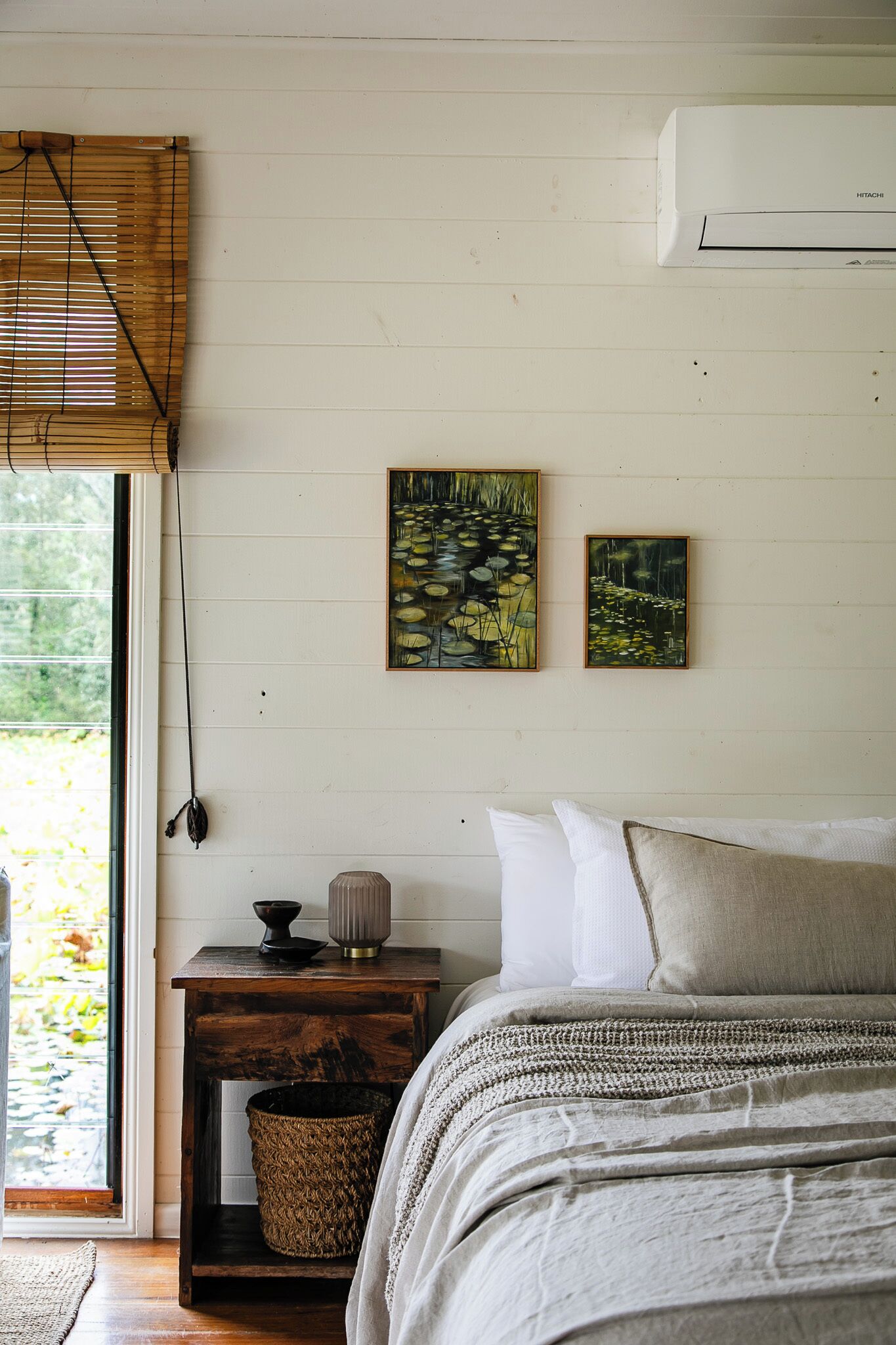Un dormitorio con cama, mesita de noche, lámpara y dos cuadros en la pared.