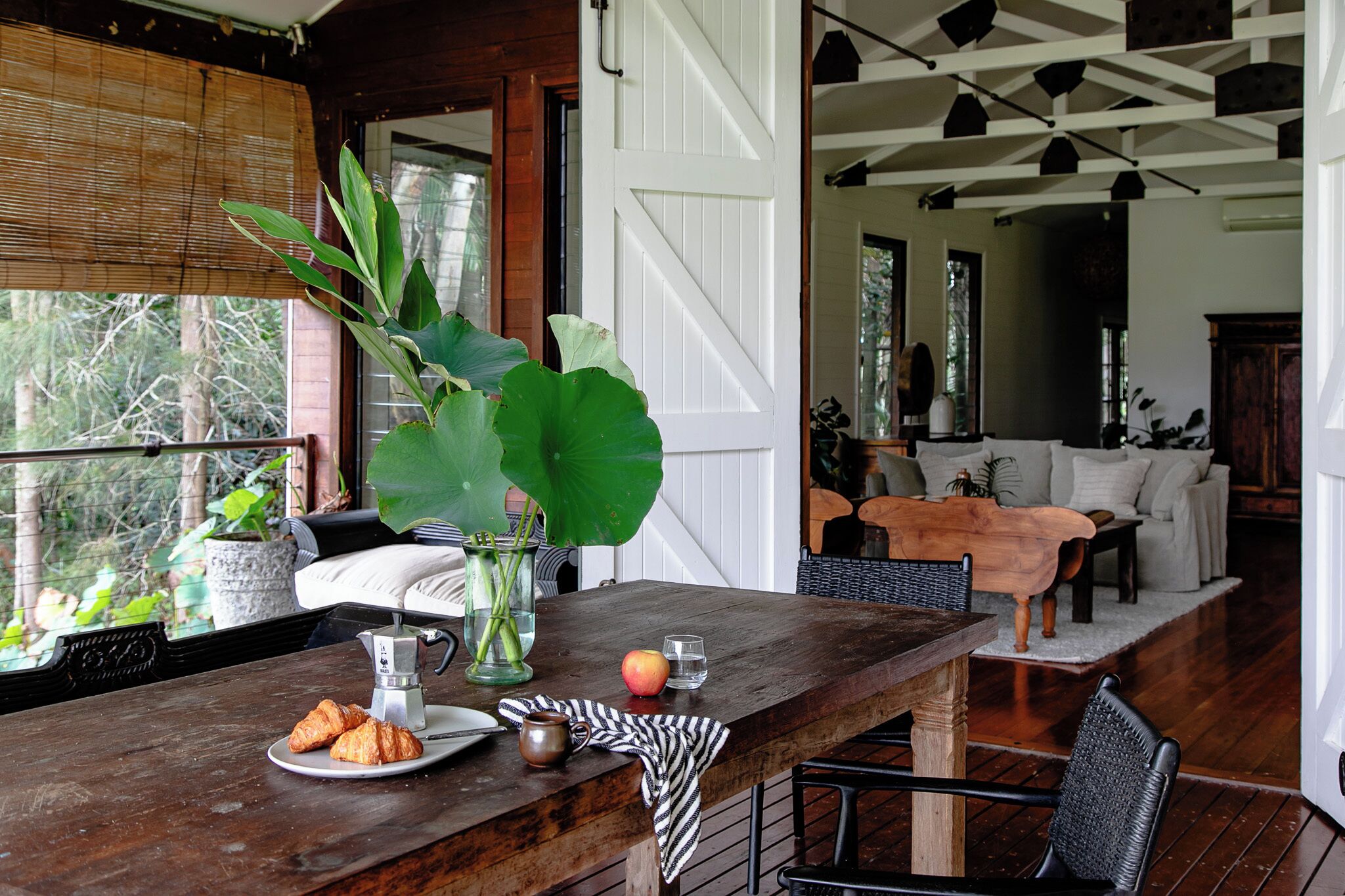 A wooden bar area with a rustic design, a large green plant, and a dining setup in the background.