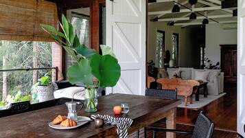 A wooden bar area with a rustic design, a large green plant, and a dining setup in the background.