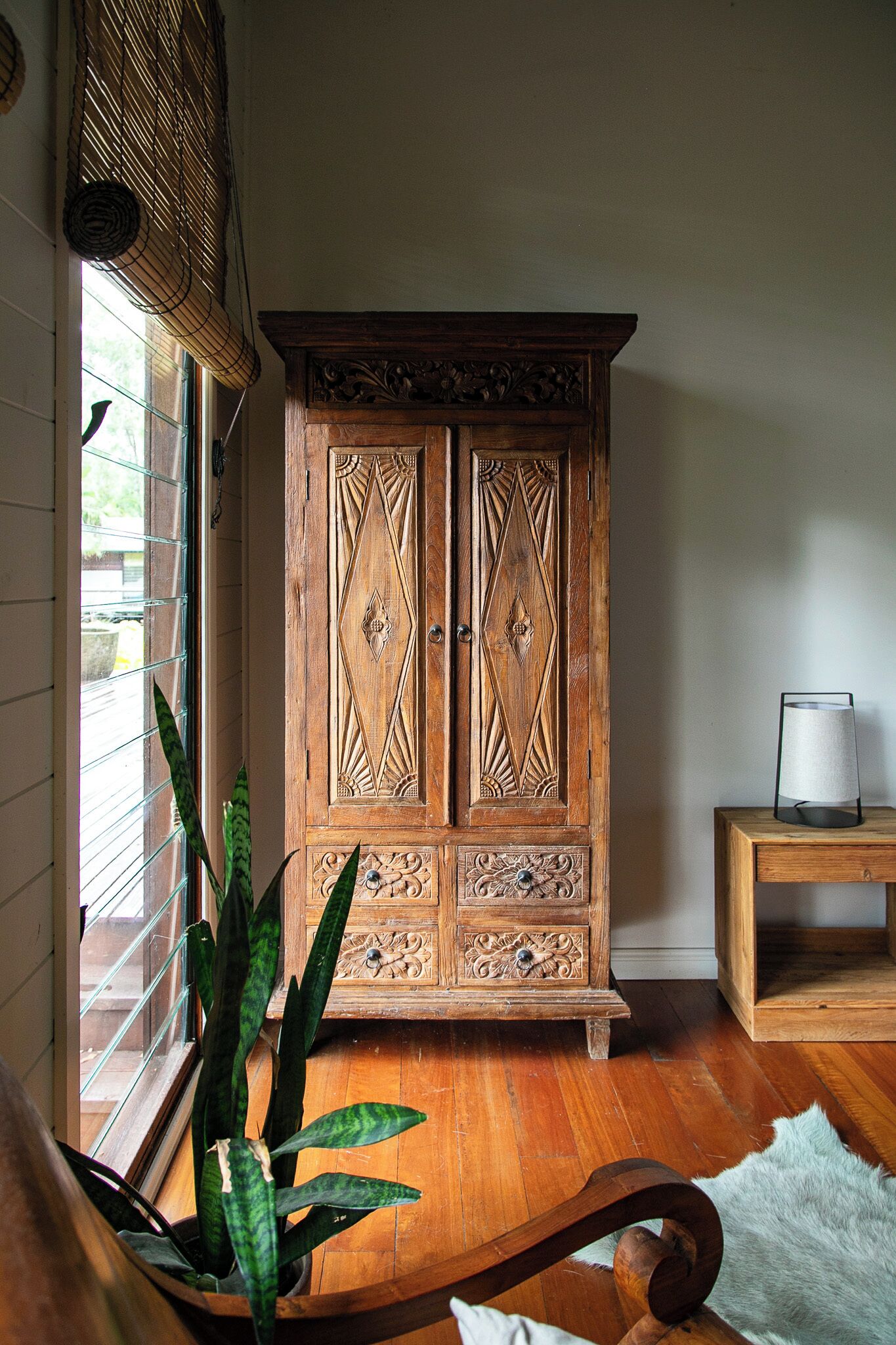 A wooden cabinet with intricate carvings, a potted plant, and a lamp on a wooden table.