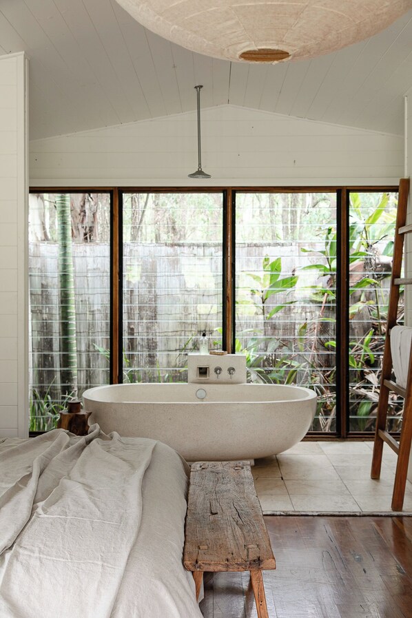 Un dormitorio con un ventanal grande, una bañera y un banco de madera.