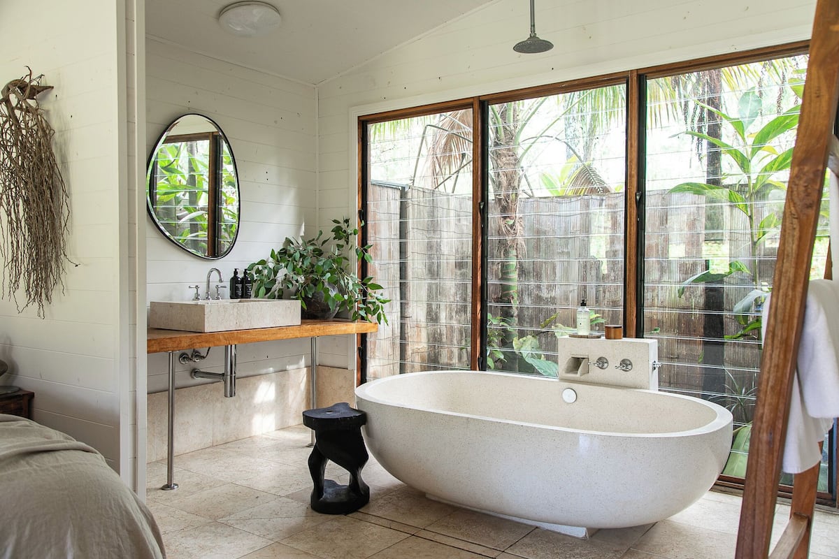 Une salle de bain avec une baignoire sur pieds, un meuble-lavabo en bois, un miroir et une plante en pot.