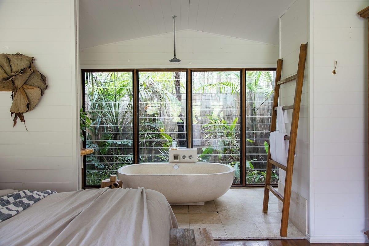 Une salle de bain avec une baignoire sur pieds, une échelle en bois et une grande fenêtre donnant sur un paysage verdoyant.
