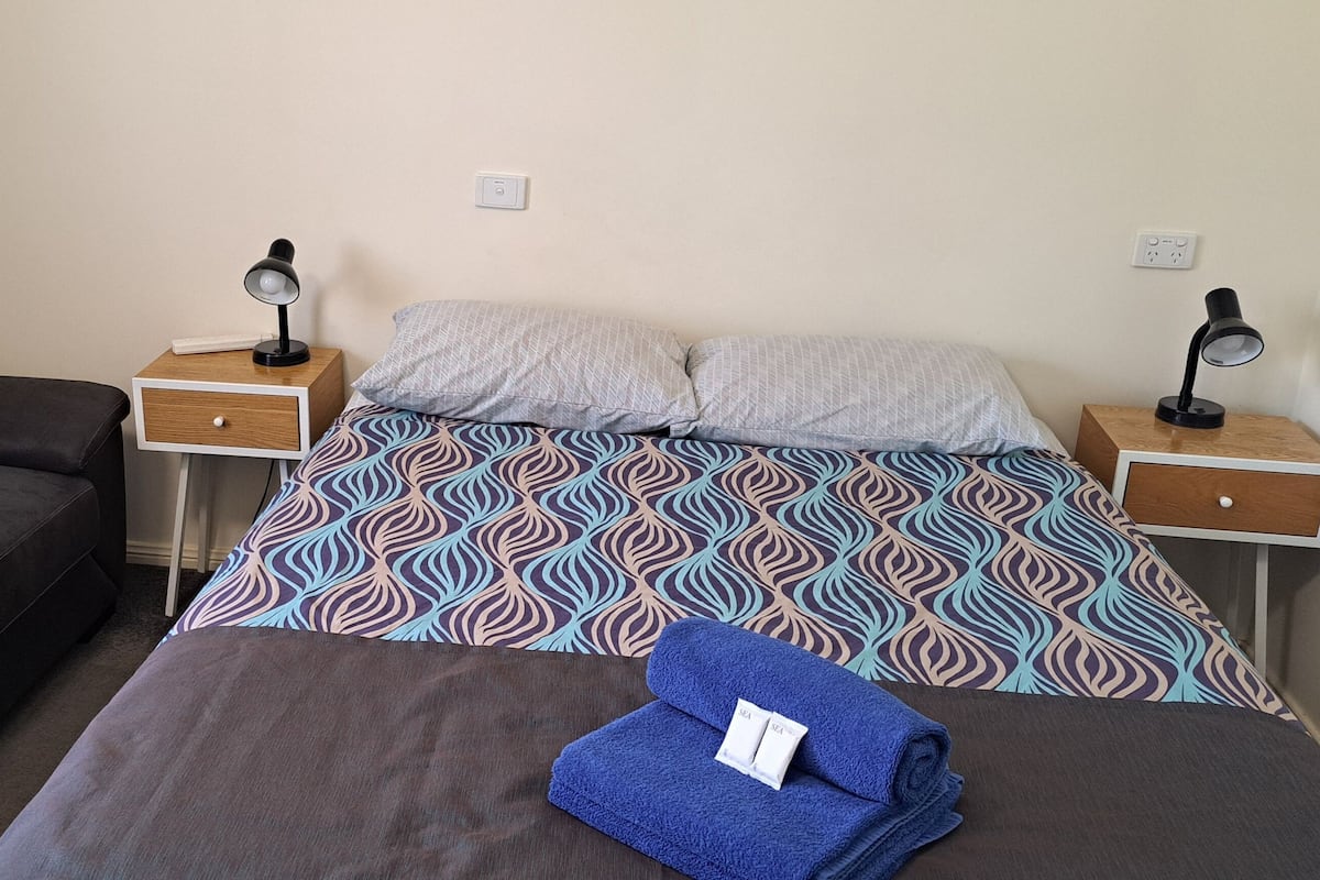 A hotel room with a bed, a sofa, two bedside tables with lamps, and a window with curtains.