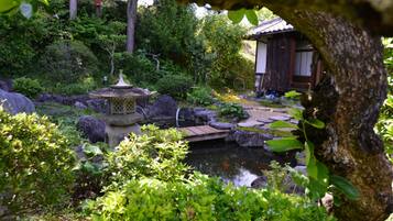 Een traditionele Japanse tuin met een stenen lantaarn, een vijver met koi karpers en een houten gebouw.