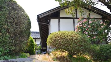 Il s'agit d'un bâtiment japonais traditionnel, doté d'une façade en bois et de murs blancs, entouré de jardins bien entretenus et d'un sentier pavé de pierres.