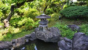 A traditional Japanese stone lantern on a rock by a pond, surrounded by lush greenery and trees.