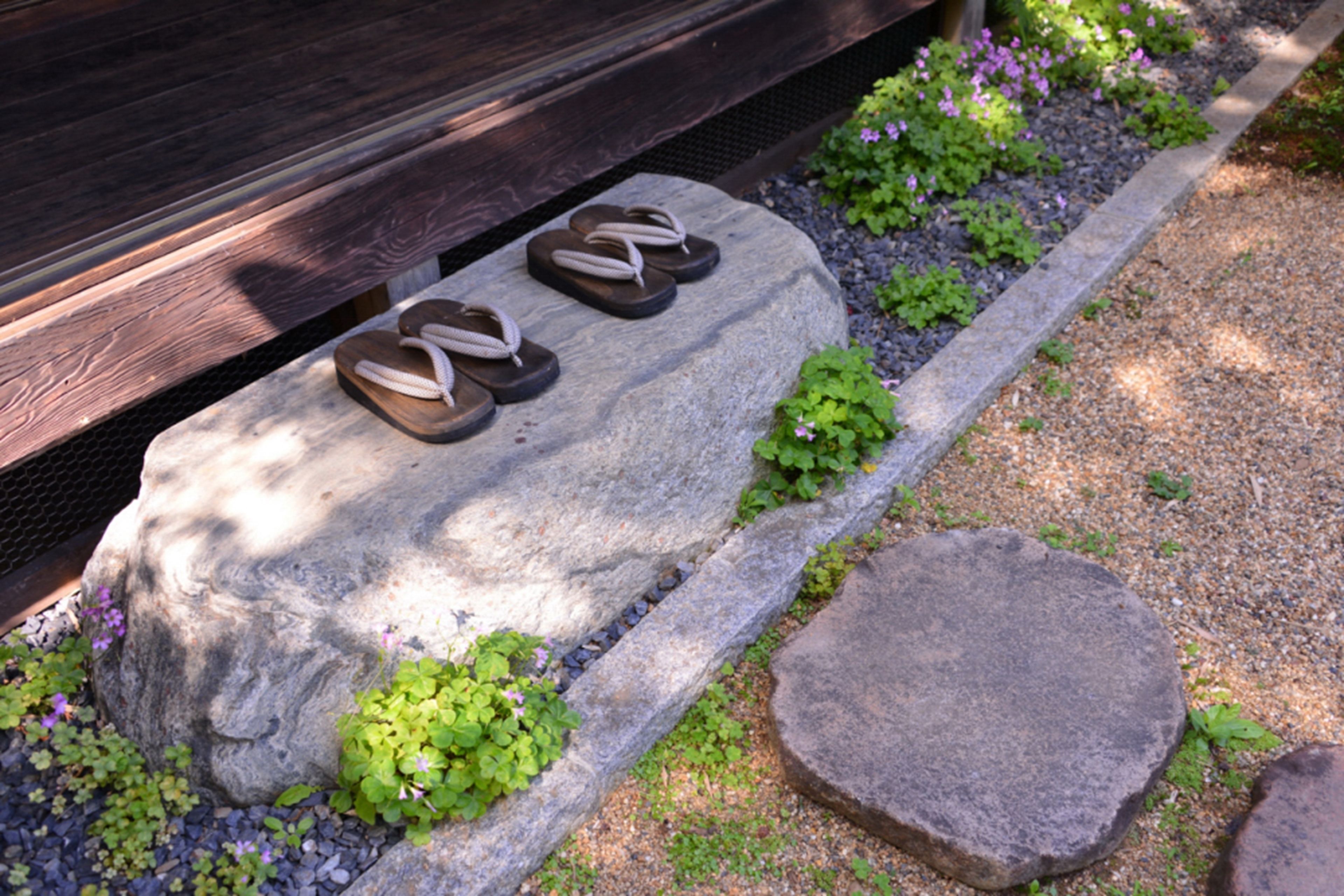 Un banc en pierre sur lequel sont posées des sandales, entouré de petites plantes et de galets.