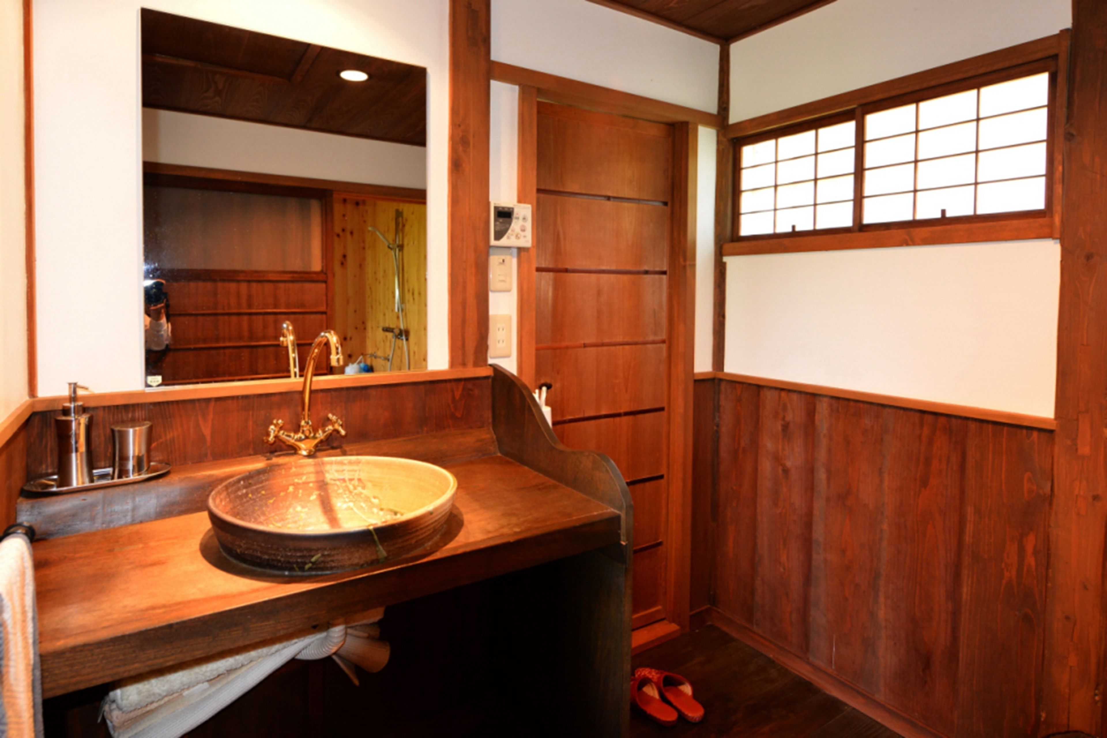 Een traditionele Japanse badkamer met een houten wastafel, een rond wasbakje en een grote spiegel.