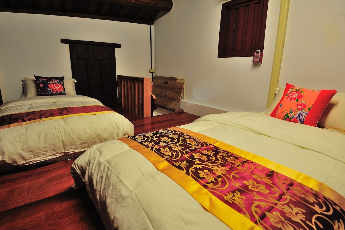 A hotel room with two beds, wooden flooring, and a wooden door.