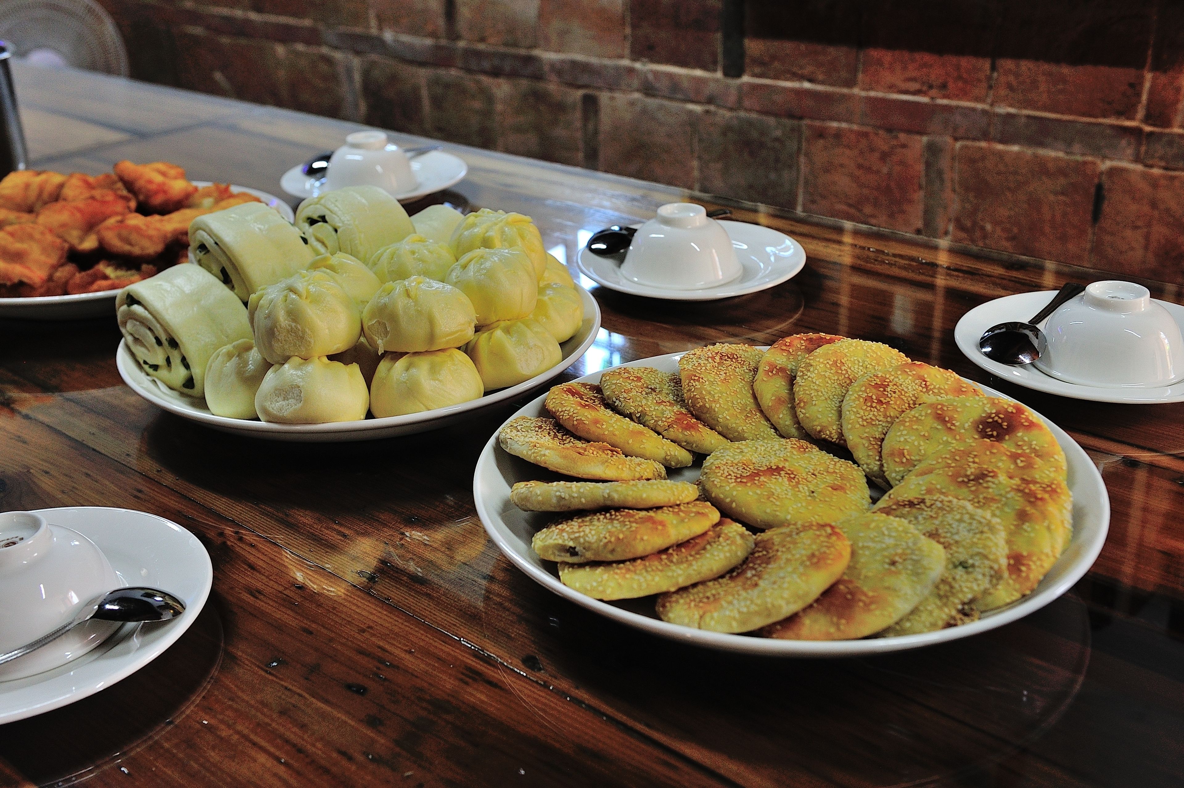 A table with various food items including rolls, bread, and fried items, along with small white cups and spoons.