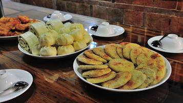 A table with various food items including rolls, bread, and fried items, along with small white cups and spoons.